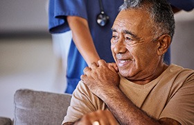 a person wearing scrubs putting their hand on a patient’s shoulder to comfort him 