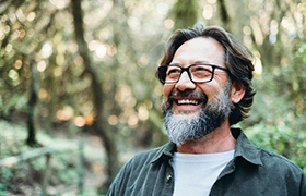 a smiling man with glasses standing outside