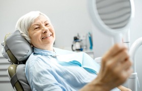 woman with dentures admiring her new smile in a mirror