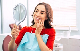 Woman with dental implants in Aurora smiling and using mirror