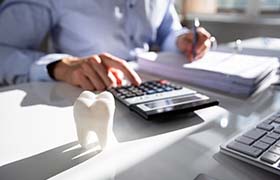 person typing on a calculator with a fake tooth on their desk