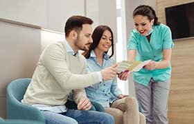 dental team member explaining the cost of dental implants to two patients