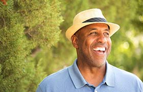 man in a blue polo shirt and fedora smiling in nature