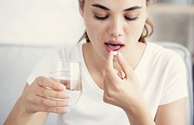 young woman in white shirt taking pill with water 