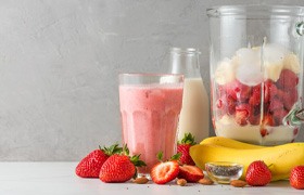 Smoothie next to pile of fruit and blender