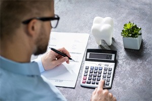 A white tooth in front of a man calculating dental costs