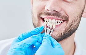 dentist holding veneers in Aurora up to patient’s smile 