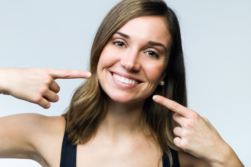 a happy young woman pointing to her smile