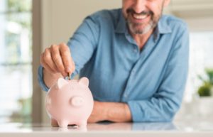 man putting coins into a pink piggy bank that he saved by getting dental implants in Aurora 