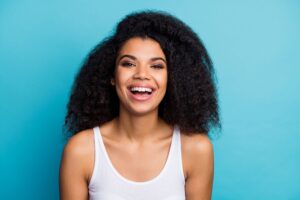 Woman in white tank top with a big smile in front of a light blue background