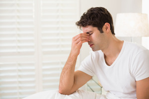 Man in white shirt sitting up in bed and rubbing his eyes